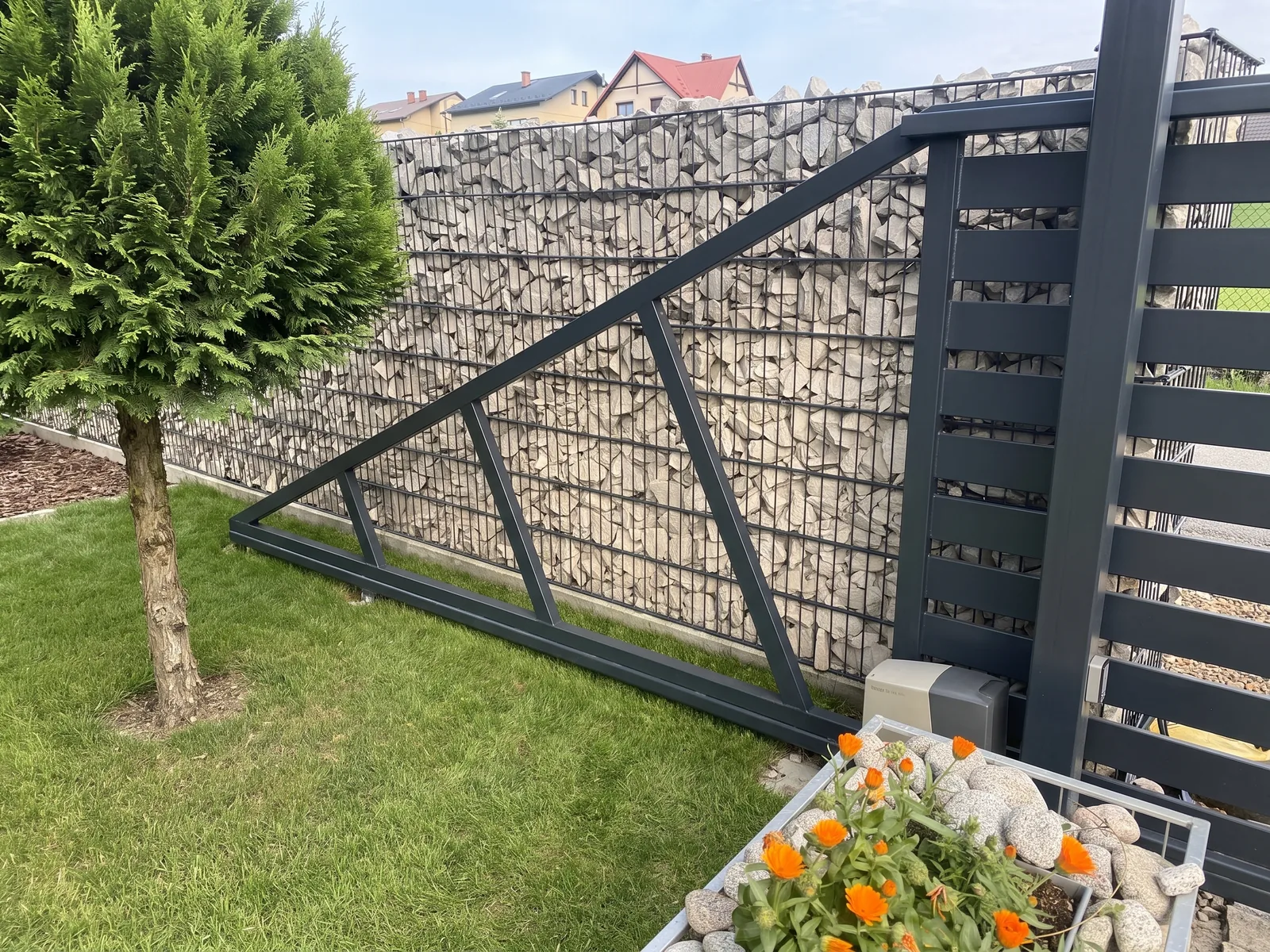 Gabionenzaun mit hellem Stein neben einem Schiebetor